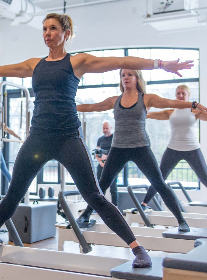 A bodybar pilates studio class with multiple people in the jumping jack formation.