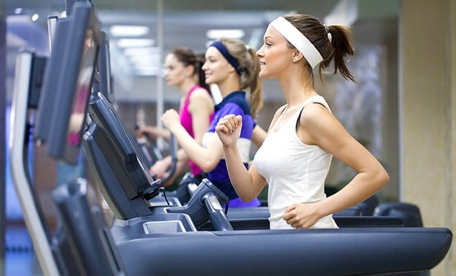 Three women exercise on treadmills indoors, wearing athletic clothing and headbands, focused on their workout.
