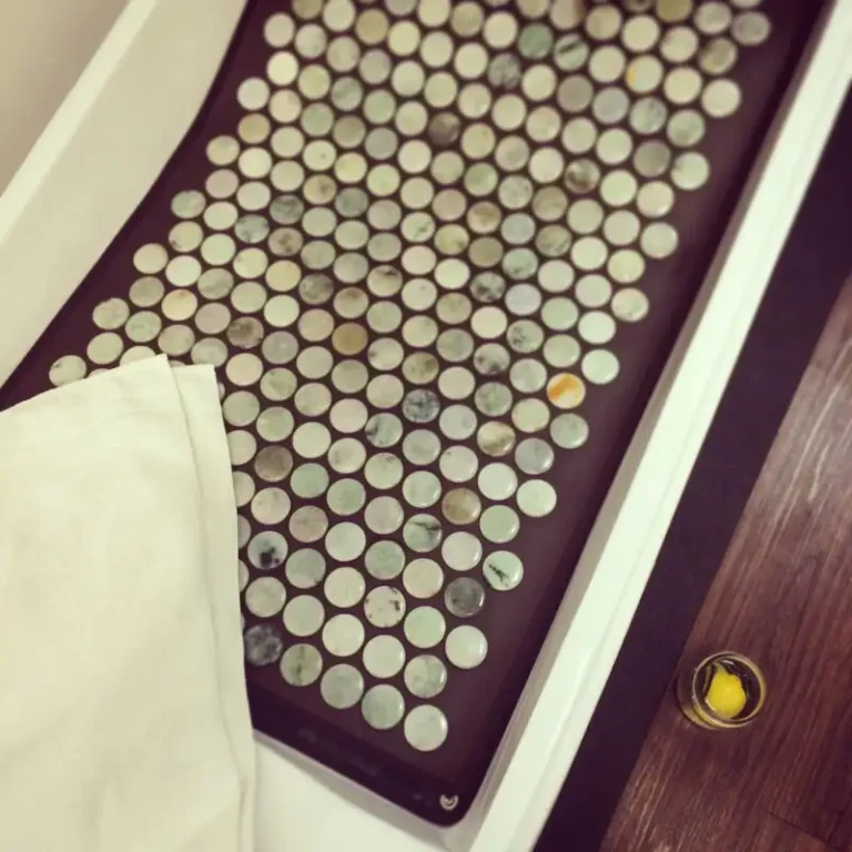 A jade stone mat with circular stones is on the floor, partly covered by a towel; a glass with lemon water is nearby.
