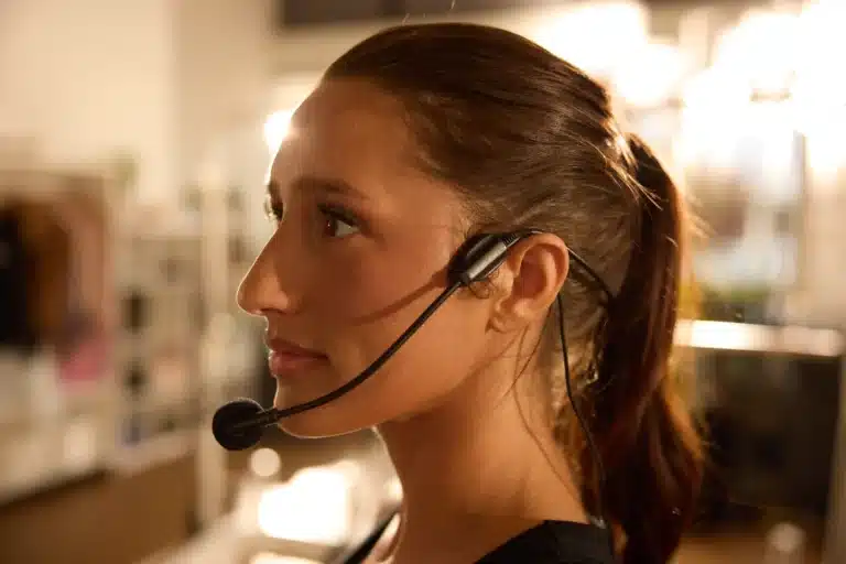 Woman with brown hair in a ponytail wearing a headset with a microphone, looking to the left.