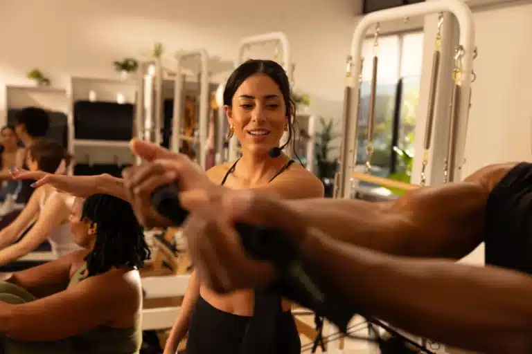 A fitness instructor wearing a headset coaches a class using resistance bands in a well-lit studio.
