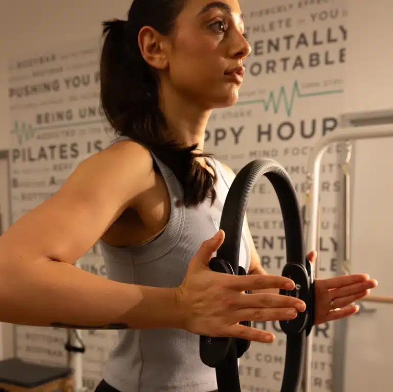 Woman in workout clothes using a Pilates ring, exercising indoors with motivational text on the wall behind her.