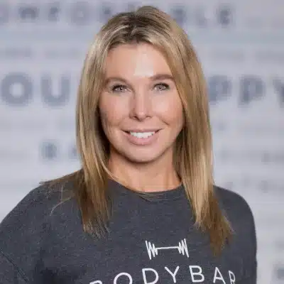 Smiling woman with straight blonde hair wearing a dark shirt that says “BODYBAR” in white text on the front.
