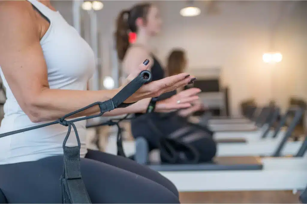 Close-up of women using pilates reformer machines in a fitness studio, focusing on arms and equipment straps.