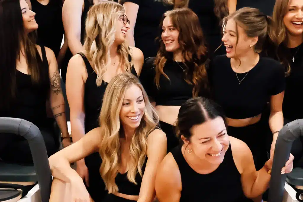 A group of women in black outfits sit and laugh together, appearing happy and enjoying each other’s company.