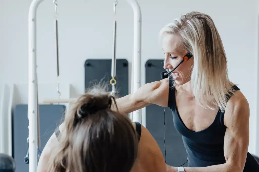 Fitness instructor with headset guiding a person during a workout session in a gym or fitness studio.