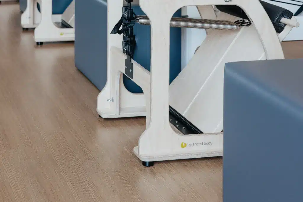 Close-up of Pilates reformer machines with padded seats on a wooden floor in a fitness studio.