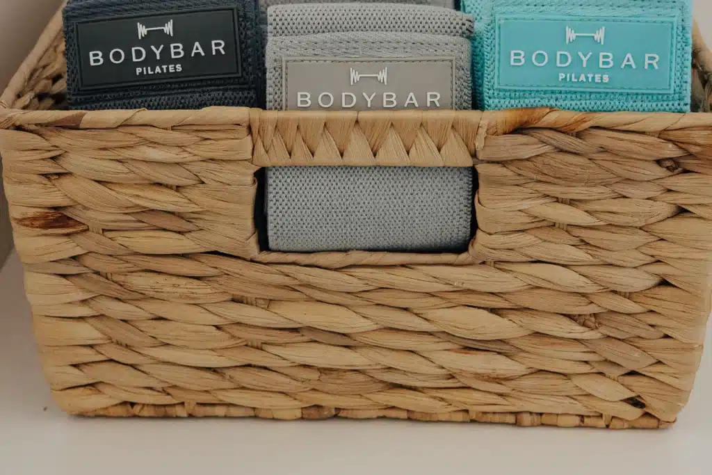 Woven basket holding three BODYBAR Pilates resistance bands in gray and teal colors.