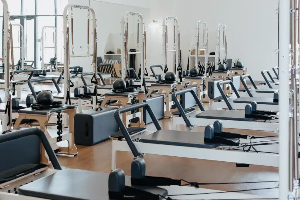 A bright Pilates studio with several reformer machines arranged neatly on a wooden floor.