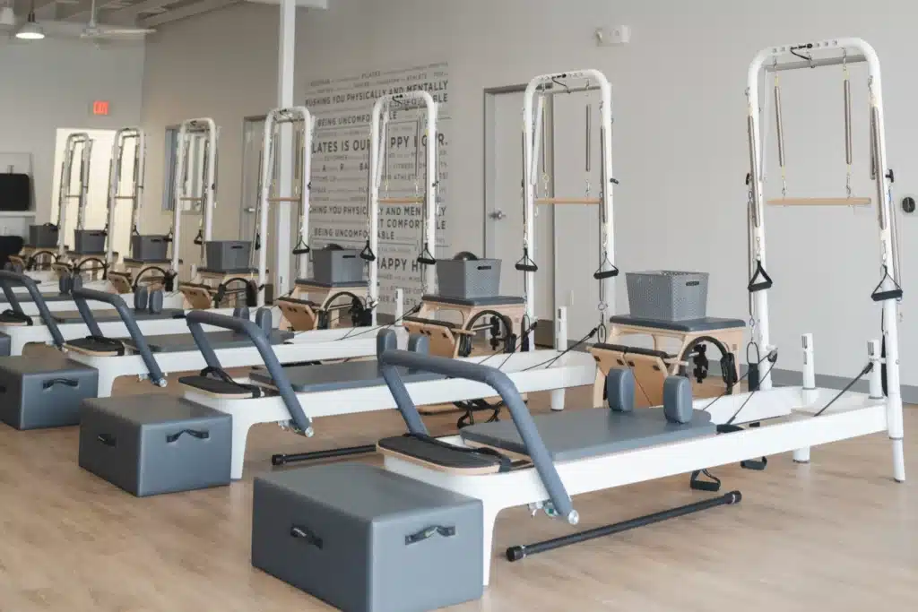A row of Pilates reformer machines in a bright, modern fitness studio with wooden floors and wall art.