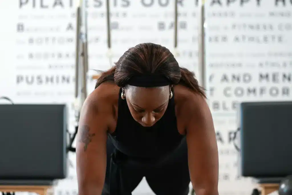 Woman in a black tank top doing a plank exercise indoors, with Pilates equipment in the background.
