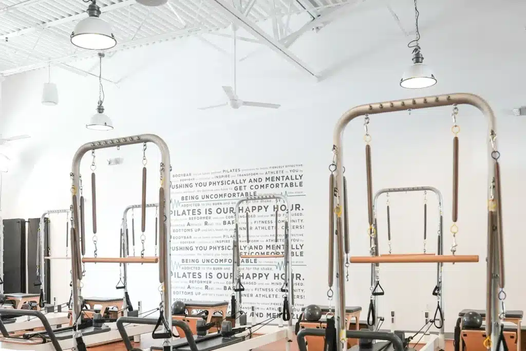 Bright Pilates studio with reformer machines, white walls, motivational quotes, and modern lighting hanging from the ceiling.