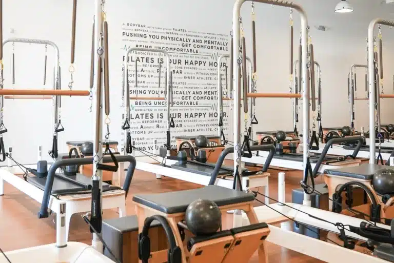 A bright Pilates studio with reformer machines arranged in rows and motivational words on the back wall.