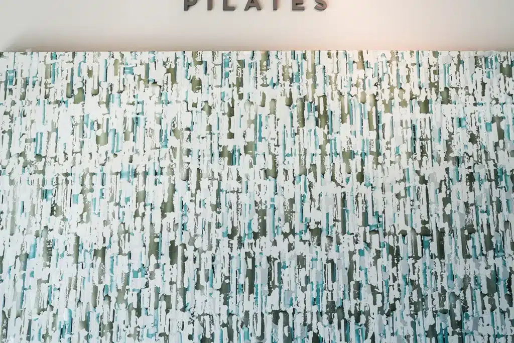 Abstract textured wall with vertical blue, green, and white patterns, partial “PILATES” sign visible at the top.