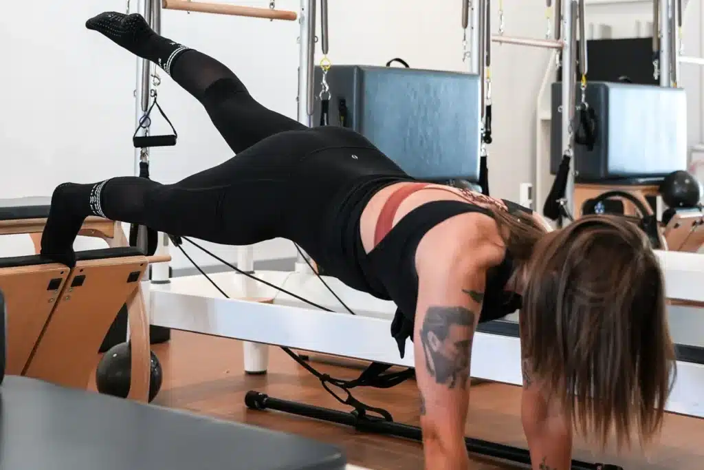 Person in black workout clothes practicing Pilates on a reformer machine in a fitness studio.
