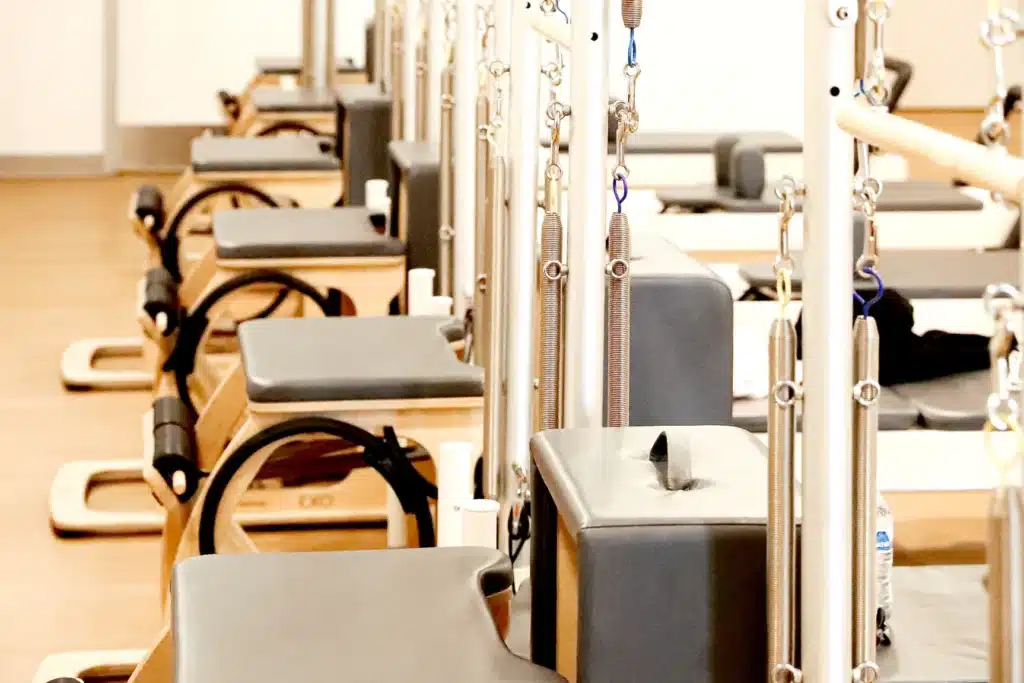 A row of Pilates reformer machines in a bright, clean studio with wooden floors.