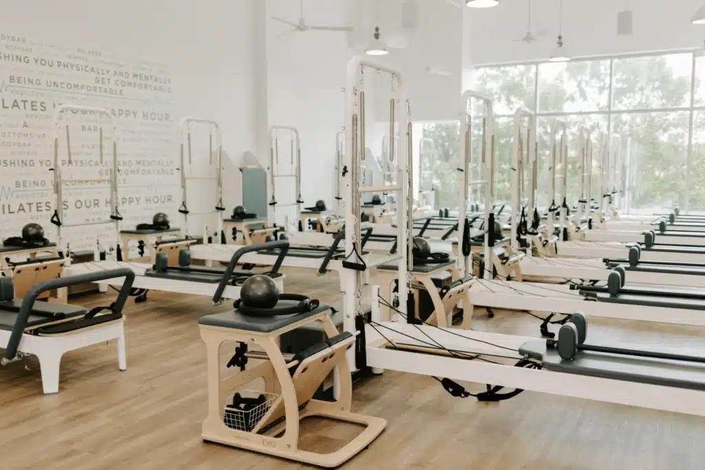 A bright Pilates studio with several reformer machines arranged in rows on a wooden floor.