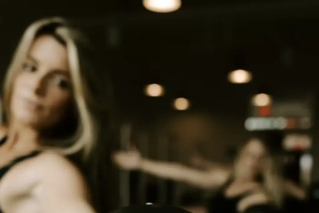 Blurry image of women in athletic wear with arms outstretched, standing in a gym or fitness studio with dim lighting.