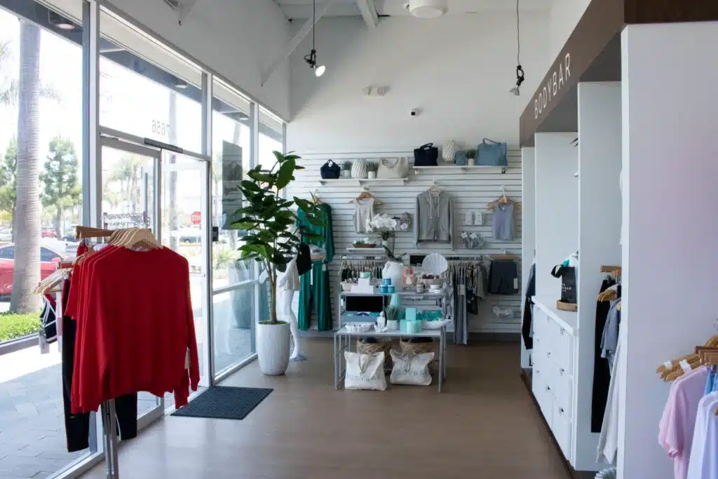 Modern clothing boutique with natural light, racks of clothes, and folded items displayed on shelves and tables.