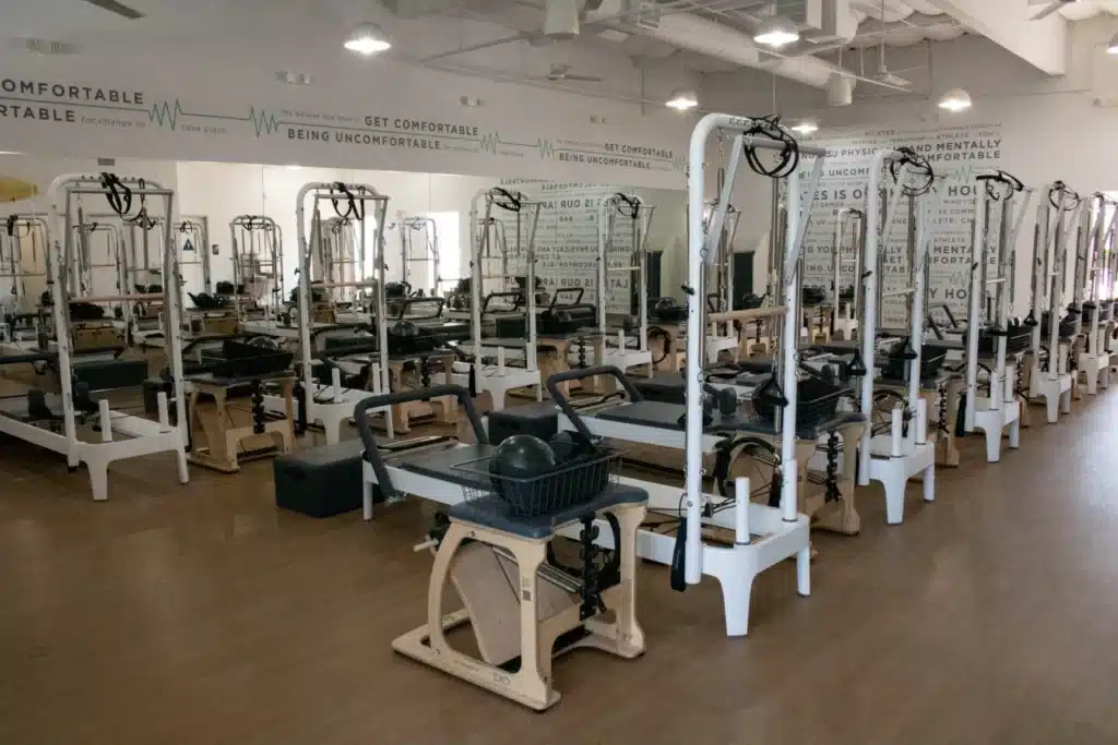 A Pilates studio with multiple reformer machines and mirrors on the wall, all equipment neatly arranged.