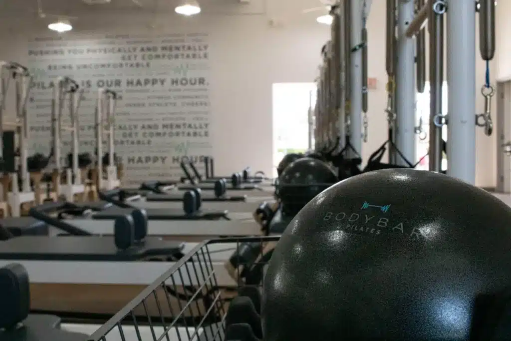 A row of Pilates reformer machines and exercise balls in a bright fitness studio with motivational quotes on the wall.