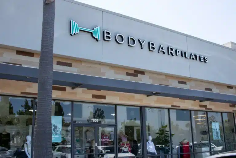 Exterior of BODYBAR Pilates studio with a sign, glass doors, and mannequins visible through the windows.