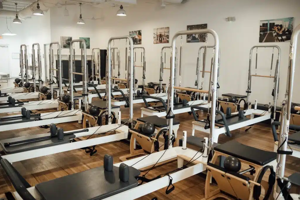 A bright Pilates studio with multiple reformer machines arranged neatly on a wooden floor.