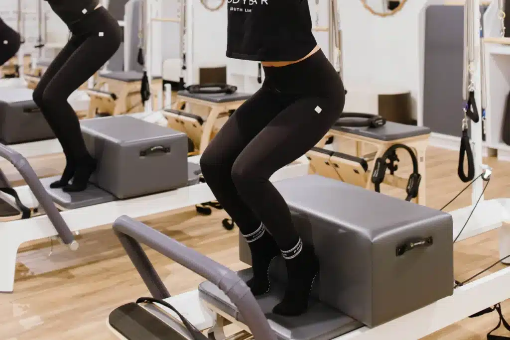 Person in black activewear balancing on a Pilates reformer in a fitness studio, focusing on their lower body.