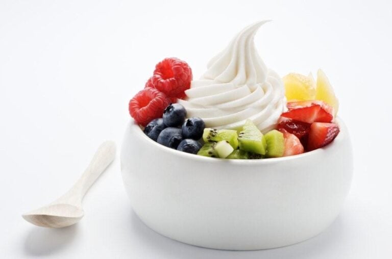 A bowl of frozen yogurt topped with raspberries, blueberries, kiwi, strawberries, and pineapple, with a spoon beside it.