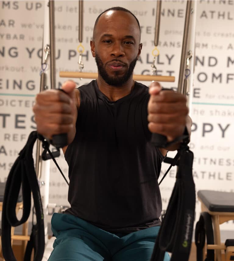 A man in a gym uses resistance bands, holding handles with both hands, facing the camera, focused on his workout.