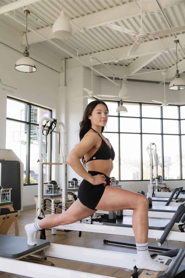 Woman performing a split lunge on a Pilates reformer in a bright BODYBAR studio